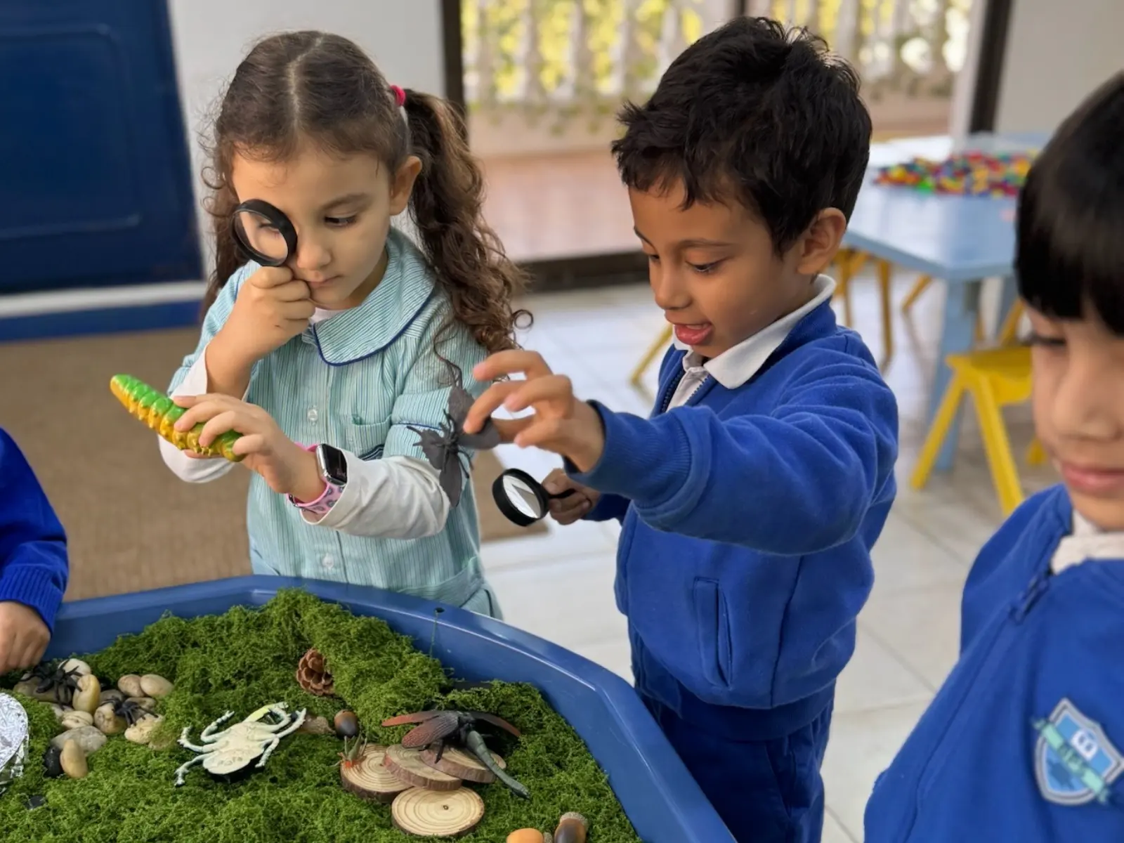 Nursery children at BPS exploring a nature tray with magnifying glasses
